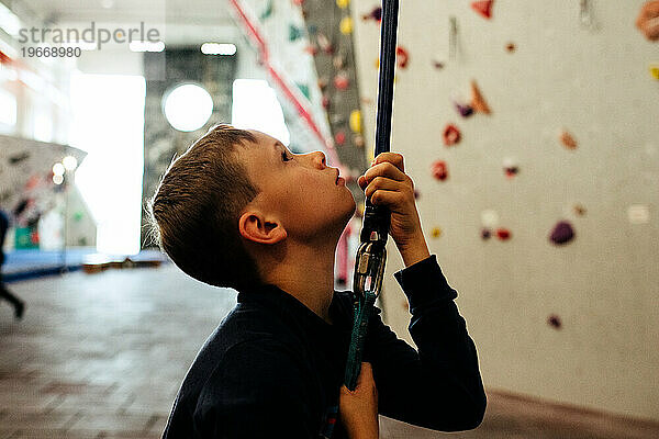 Kind hält sich an einem Kletterseil fest und ist bereit  drinnen eine Wand zu erklimmen