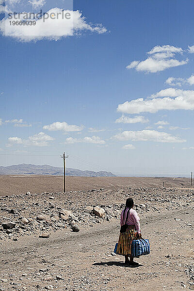 Eine Frau hält ihre Koffer in der Hand und wartet auf einen Bus in der Atacama-Wüste  Bolivien.