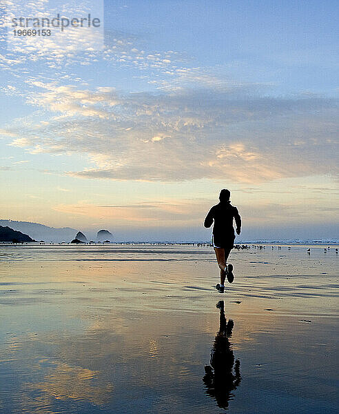 Eine Frau läuft bei Sonnenaufgang am Strand.