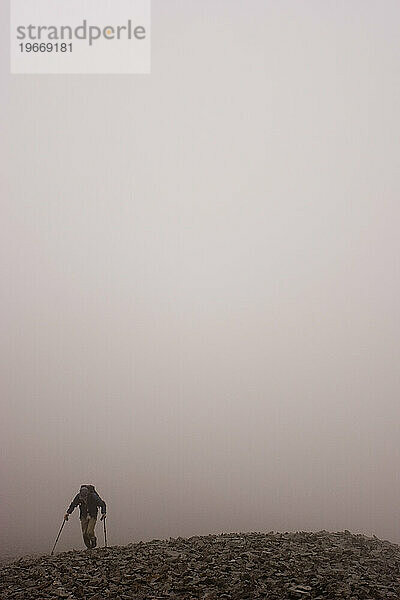 Ein einsamer Wanderer klettert durch den Nebel in der Nähe von Stony Dome im riesigen Hinterland des Denali-Nationalparks  Alaska.
