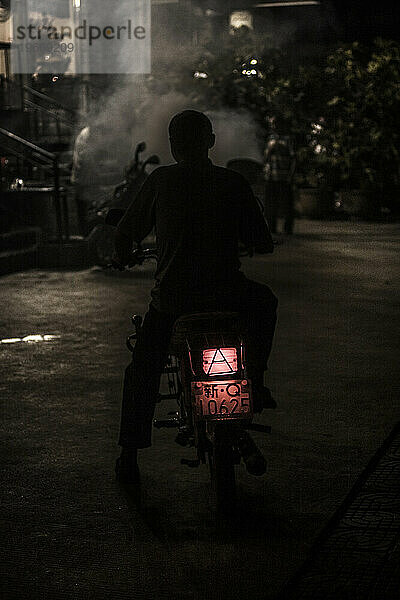 Mann verlässt nachts mit dem Motorrad ein Restaurant.