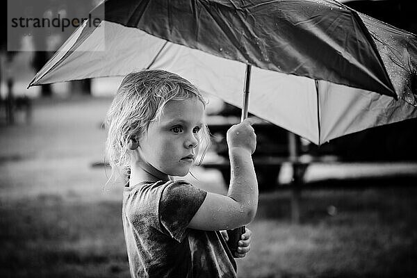 Kind steht im Regen unter einem Regenschirm