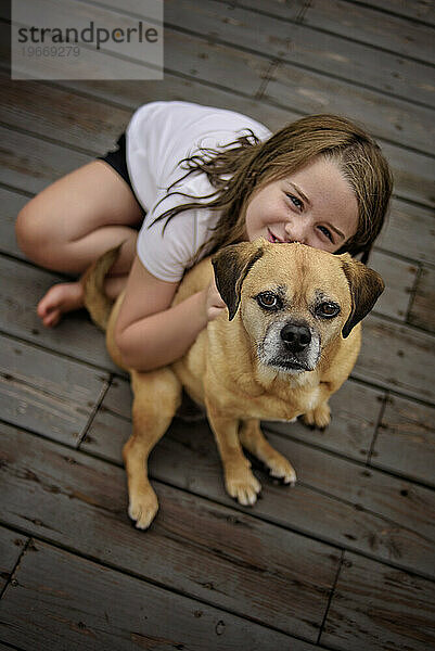 Glückliches kleines Mädchen  das draußen einen braunen Puggle-Hund streichelt