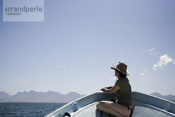 Eine Frau sitzt auf der Vorderseite eines Bootes mit Bergen in der Ferne in Loreto  Baja California Sur  Mexiko.
