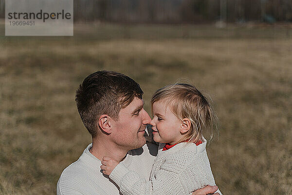 Kleines Mädchen umarmt zärtlich ihren Vater auf dem Feld  aus nächster Nähe