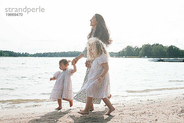 Mutter geht im Sommer mit ihren beiden Töchtern am Strand entlang