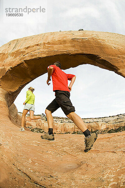Zwei Menschen laufen unterhalb des Wilson Arch in der Nähe von Moab  Utah.