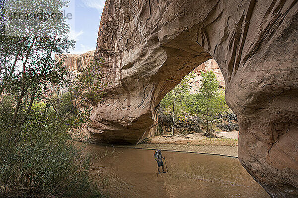 Eine Person steht in einem Bach unter einem natürlichen Felsbogen.
