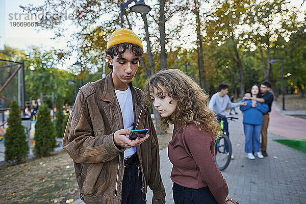 Mann und Mädchen schauen im Park auf das Telefon