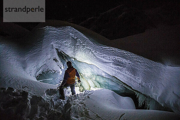 Silhouette eines Bergsteigers  der nachts die Eishöhle betritt