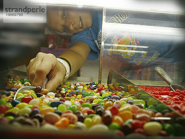 Eine jüngere Angestellte in einem Süßwarenladen schaufelt für einen Kunden Gummibärchen.