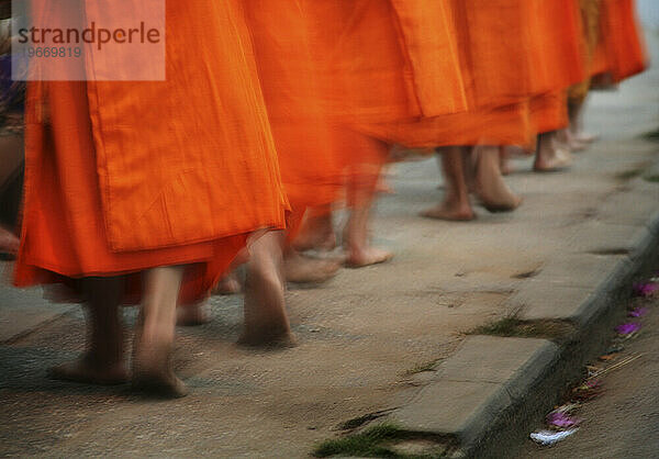 Die Füße buddhistischer Mönche gehen in einer Reihe auf einem Bürgersteig. Luong Probang  Laos.