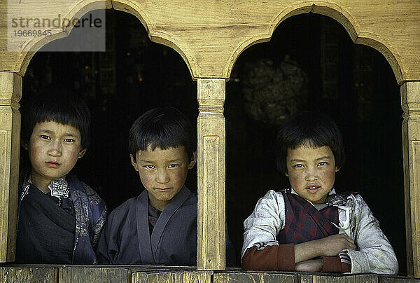 Drei Jungen schauen in Paro  Bhutan  aus einem Fenster.