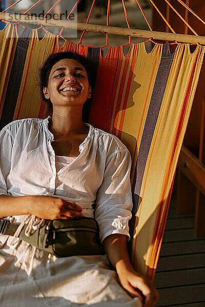 Junge glückliche Frau liegt auf einer farbig gestreiften Hängematte.