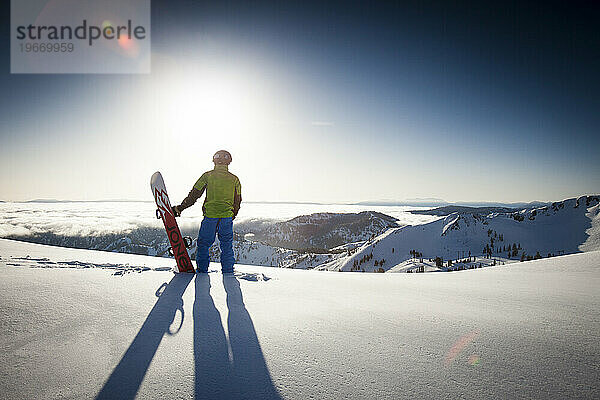 Eine männliche Snowboarder-Silhouette mit Blick auf Berge und Neuschnee.