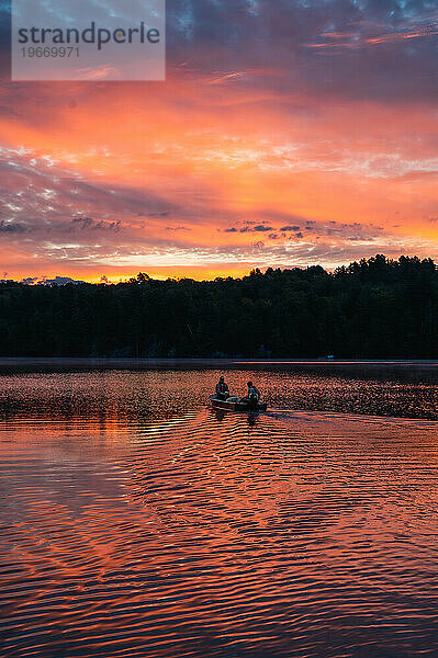 Zwei Personen in einem Fischerboot fahren bei Sonnenaufgang über einen See.