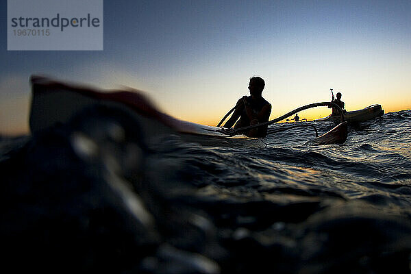 Silhouette von drei Auslegerkanu-Paddlern bei Sonnenuntergang aus der Perspektive eines niedrigen Winkels.