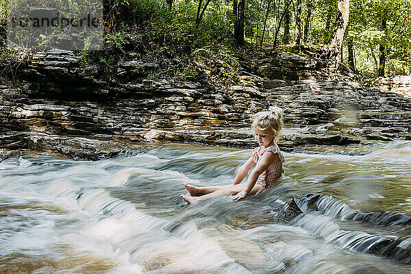 Kind sitzt in einem ruhigen  malerischen  fließenden Wasserfall im Wald