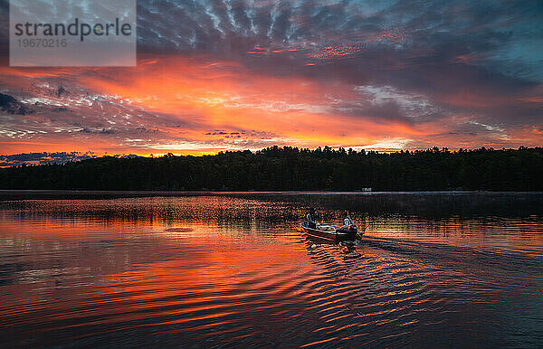 Zwei Personen in einem Fischerboot fahren bei Sonnenaufgang über einen See.