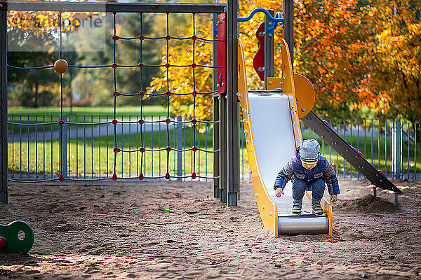 Entzückender kleiner Junge  der sich im Herbst auf einem Spielplatz vergnügt