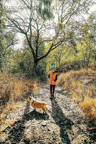 Ein Junge geht mit einem Corgi-Hund im Herbstwald spazieren