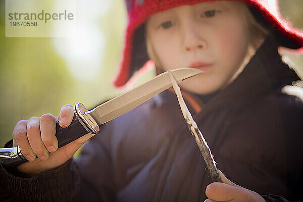 Ein Junge schnitzt mit einem Jagdmesser.