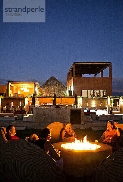Eine Gruppe von vier Personen genießt ein Feuer  während die Sonne in einem Resort untergeht.