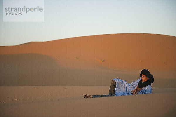 Ein Wüstenjunge sitzt bei Sonnenaufgang auf der Spitze einer Sanddüne.