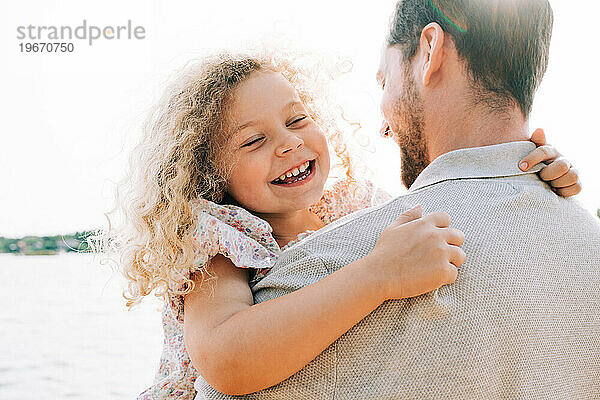 Vater und Tochter lachen gemeinsam am Strand