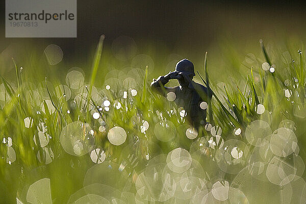 Ein Spielzeugsoldat späht durch das mit Morgentautropfen bedeckte Gras.