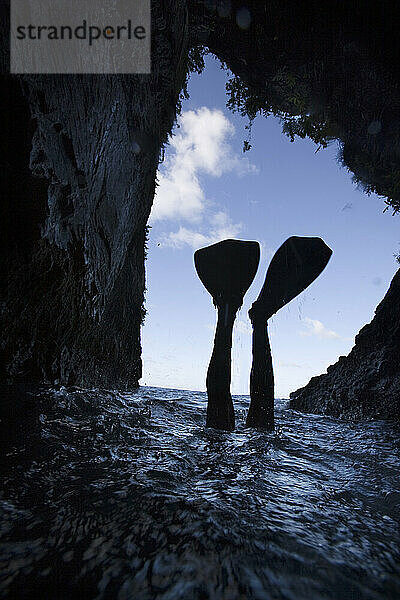 Die mit Flossen bekleideten Füße eines Höhlentauchers tauchen unter der Wasseroberfläche ab und zeichnen sich als Silhouette vor dem blauen Himmel ab  der durch eine Höhlenöffnung in Costa Rica zu sehen ist.