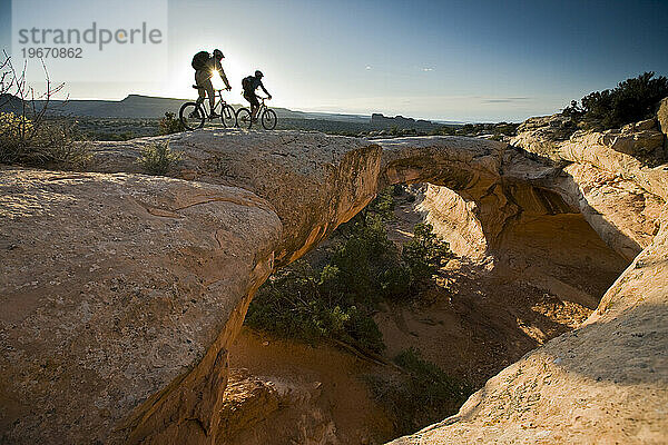 Ein Mann und eine Frau reiten über einen natürlichen Felsbogen in der Wüste in der Nähe von Moab  Utah.