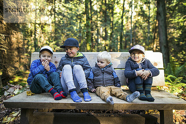 Vier kleine Kinder sitzen und ruhen sich auf einer Parkbank aus.