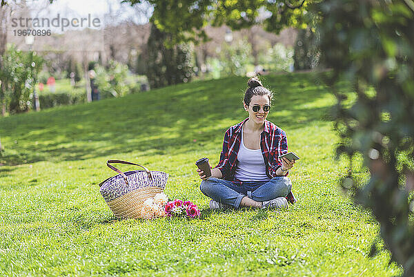 Vorderansicht einer jungen Hipster-Frau  die auf Gras in einem Park sitzt