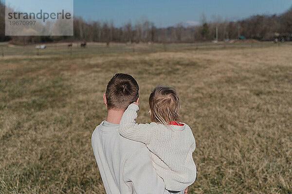 Ein Mann umarmt ein kleines Kind fest auf einem trockenen Feld  Rückansicht
