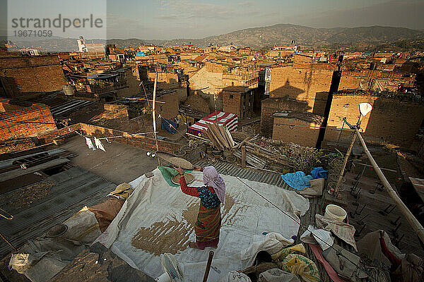 Eine einheimische nepalesische Frau siebt Getreide auf einem Dach in einer indischen Stadt.