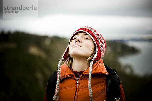 Eine junge Frau legt den Kopf zurück und genießt das kühle Wetter beim Wandern im Nordwesten.