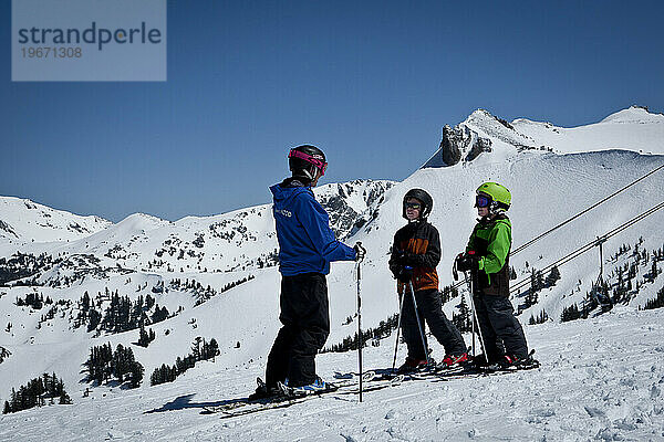 Zwei junge Skifahrer mit ihrem Skilehrer blicken auf eine weite Aussicht.