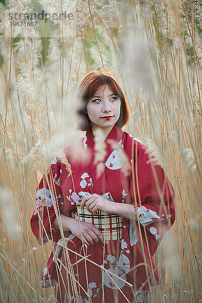 Mädchen im roten Kimono schaut im Schilf nach oben