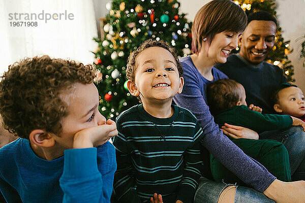 Gemischtrassiges Kleinkind lächelt mit Familie mit Weihnachtsbaum
