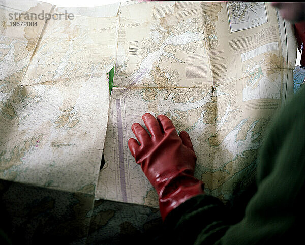 Ein Mann mit roten Handschuhen schaut auf eine Karte  während er auf einem Boot in den Gewässern des Prince William Sound in Alaska sitzt.