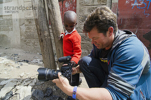 Fotograf zeigt einem kleinen Jungen  wie er seine Kamera benutzt  Kenia  Afrika