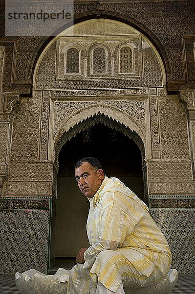 A man wearing traditional Middle Eastern clothing sits in one of the decorative gardens of a mosque.