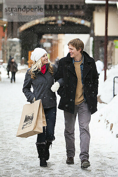 Junges attraktives Paar beim Einkaufen in einem Dorf bei fallendem Schnee.