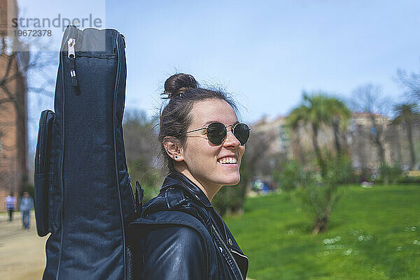 Seitenansicht einer jungen lächelnden Hipster-Frau  die in einem Park spaziert