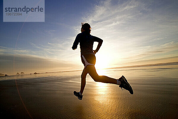 Eine Frau joggt während eines wunderschönen Sonnenuntergangs über den nassen Sand.