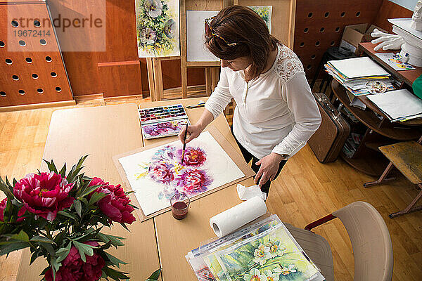 Die Künstlerin arbeitet in ihrem Atelier  malt einen Strauß Pfingstrosen  Draufsicht