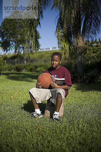 A portrait of a young boy holding a basketball and a book in green grass.