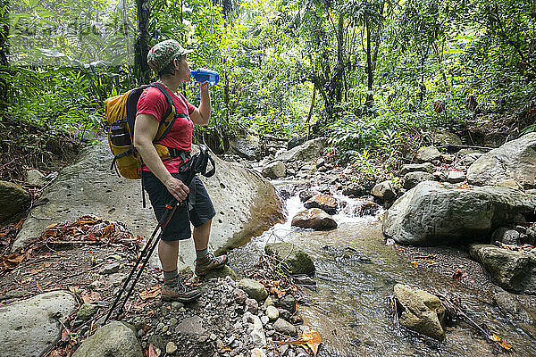 Eine Frau macht auf ihrer Wanderung auf Abschnitt 3 des Waitukubuli National Trail auf der Karibikinsel Dominica eine Wasserpause an einem Bach.