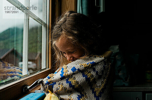 Mädchen in einem gemütlichen norwegischen Pullover  das aus dem Fenster einer Hütte schaut